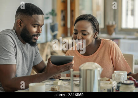 Lächelnd Afrikanische amerikanische Paar essen Frühstück und mit einem Tablet Stockfoto