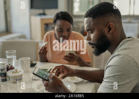 Junge afrikanische amerikanische Paar abgelenkt vom Frühstück durch ihre cellphones Stockfoto