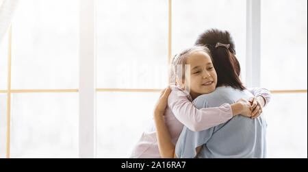 Mädchen kuscheln Mutter mit Liebe und Zärtlichkeit in der Nähe der Fenster Stockfoto