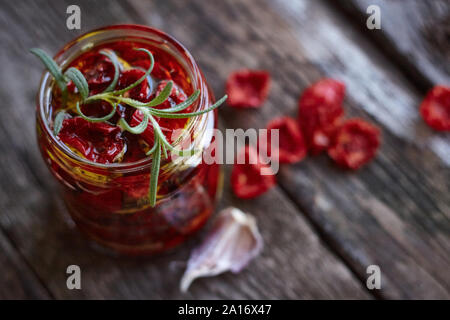 Draufsicht auf das Glas hausgemachten sonnengetrocknete Tomaten mit Kräutern der Provence, Knoblauch und Olivenöl auf eine rustikale Holz- Oberfläche, selektiver Fokus Stockfoto