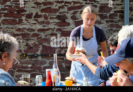Junge Frau Kellnerin serviert Burger zu Kunden außerhalb Essen an den Tischen im Restaurant in Runwayskiln Marloes Pembrokeshire Wales UK KATHY DEWITT Stockfoto
