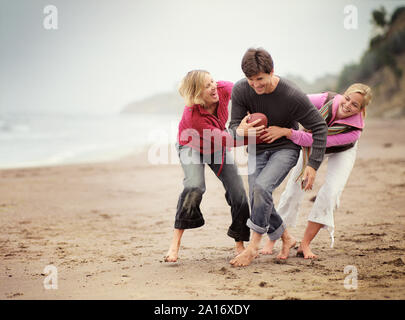 Mitte nach Paar mit Ihrer halbwüchsigen Tochter spielen ein Ballspiel am Strand. Stockfoto