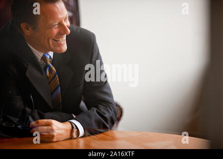 Porträt eines Geschäftsmannes lachen herzlich an einem Tisch, während seine Brille Holding. Stockfoto