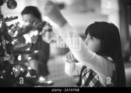 Seitliche Sicht auf ein kleines Mädchen schmücken einen Weihnachtsbaum. Stockfoto