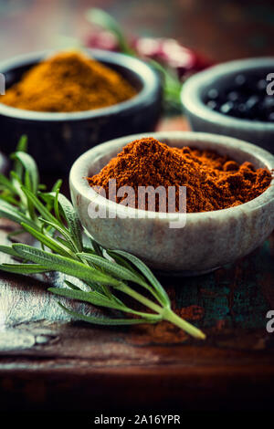 Verschiedene Gewürze in kleinen Behältern und Rosmarin auf Holz- Hintergrund Stockfoto