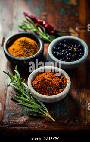 Verschiedene Gewürze in kleinen Behältern und Rosmarin auf Holz- Hintergrund Stockfoto