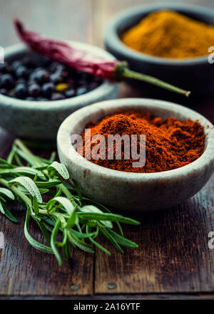 Verschiedene Gewürze in kleinen Behältern und Rosmarin auf Holz- Hintergrund Stockfoto