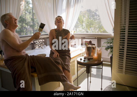 Reifen erwachsenen Paar sitzen in Handtücher neben einem Schaumbad, wie man malt die anderen im Schlamm beim Trinken von Champagner. Stockfoto
