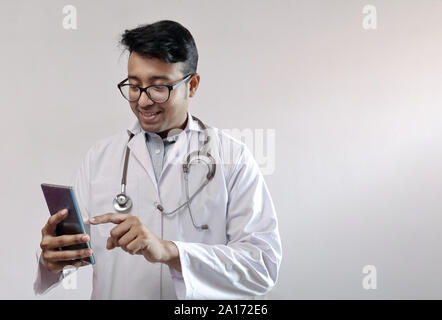 Männliche indische Arzt im weißen Kittel und Stethoskop berühren smart phone Stockfoto
