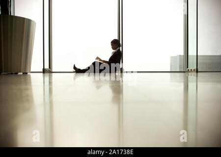 Junge Geschäftsfrau, sitzen auf dem Boden, während Sie die Zeitung lesen. Stockfoto