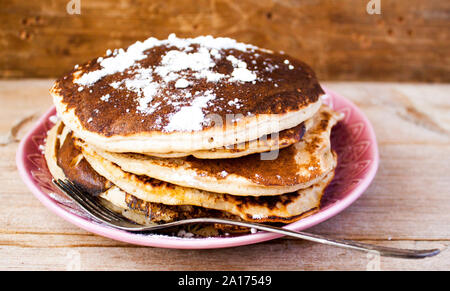 Stapel von hausgemachten sauber essen Hafer Pfannkuchen mit Zucker auf rosa Platte auf rustikalen Tisch mit alten Tafelsilber. Selektive Weichzeichner. Stockfoto