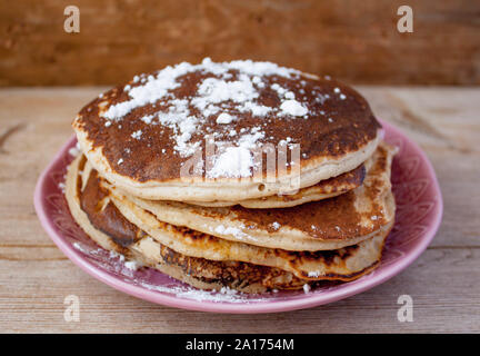 Stapel von hausgemachten sauber essen Hafer Pfannkuchen mit Zucker auf rosa Platte auf rustikalen Tisch. Selektive Weichzeichner. Fastnacht, Pfannkuchen carniv Stockfoto