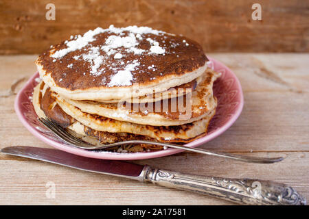 Stapel von hausgemachten sauber essen Hafer Pfannkuchen mit Zucker auf rosa Platte auf rustikalen Tisch mit alten Tafelsilber. Selektive Weichzeichner. Stockfoto