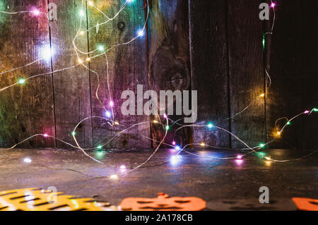 Farbe LED Girlande auf eine Holzwand und Kürbisse von orange Papier auf den Tisch gehauen. kopieren. Basteln für Halloween Feier Konzept. Handarbeit. Stockfoto