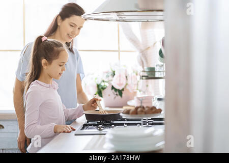 Kleines Mädchen lernen, wie man unter Aufsicht der Mutter zu kochen Stockfoto