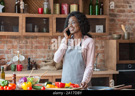 Junge Frau mit angenehmen Gespräch am Telefon, beim Kochen Stockfoto