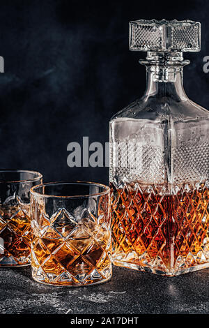 Gläser der Whiskey mit einem quadratischen Dekanter auf einem schwarzen Stein. Stockfoto