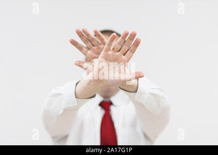 Schockiert und entsetzt Menschen verbietet, die Bilder von sich. Portrait des jungen Mannes in Hemd und roter Krawatte bedeckte sein Gesicht mit der Hand und kam Stockfoto