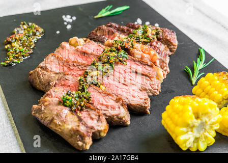 In Scheiben geschnitten mittlere Rib Eye Rindersteak mit Fleisch mit Chimichurri auf schwarzem Hintergrund Stockfoto