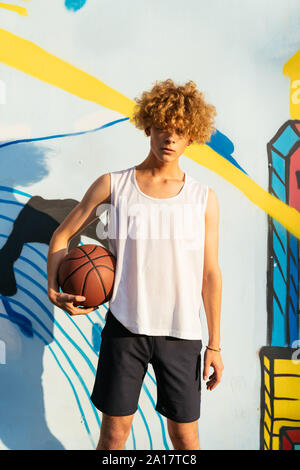 Junge Männer mit kurvigen Haare holding Basketball Ball vor Graffiti Stockfoto