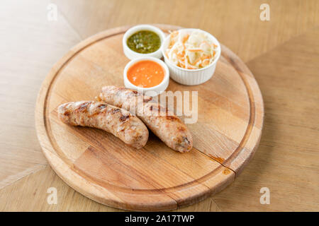 Gegrillte Würstchen. Serviert auf einem Holzbrett. Grill Restaurant Menü, eine Reihe von Fotos von verschiedenen Fleischsorten. Sauerkraut und zwei Saucen Stockfoto