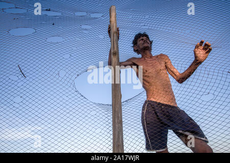 Skinny Fischer hinter einer zerrissenen Fischernetz mit einem Holz Pol Stockfoto