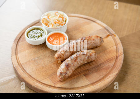 Gegrillte Würstchen. Serviert auf einem Holzbrett. Grill Restaurant Menü, eine Reihe von Fotos von verschiedenen Fleischsorten. Sauerkraut und zwei Saucen Stockfoto