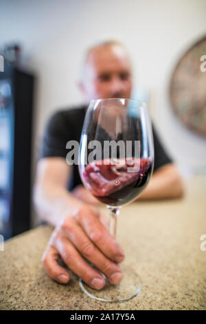 Mann wirbelt ein Glas Rotwein bei einer Weinprobe. Stockfoto