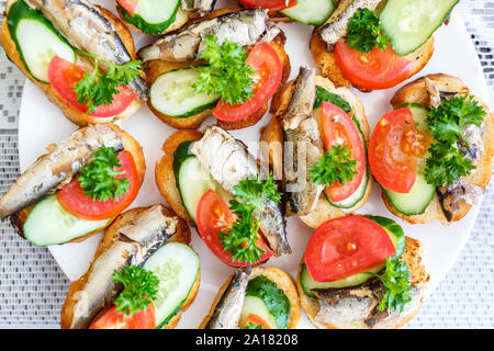 Platte von Sandwiches aus langen Laib, Sprotten, Tomaten, Gurken und Petersilie Stockfoto