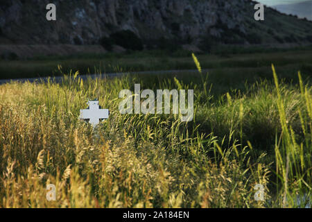 Eine weiße Kreuz ist durch das hohe Gras von einer ländlichen Straße gesehen. Stockfoto