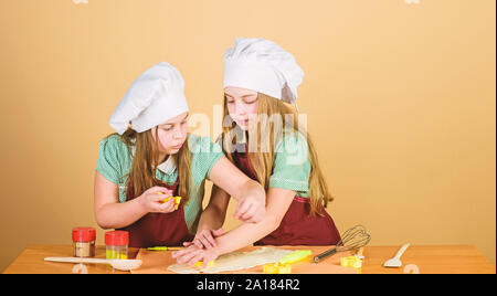 Sie kochen. Adorable kleinen Mädchen genießen zusammen kochen. Kleine Kinder Kochkurs. Niedliche Köche in kochschürzen Gestaltung der Figuren aus Teig mit Schimmel. Stockfoto