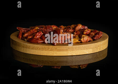 Menge ganze trockene rote Chili peperoncino auf Bambus Platte auf schwarzem Glas isoliert Stockfoto