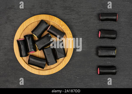 Menge ganz süßen schwarzen Lakritz Bonbons auf Bambus Untersetzer flatlay am grauen Stein Stockfoto