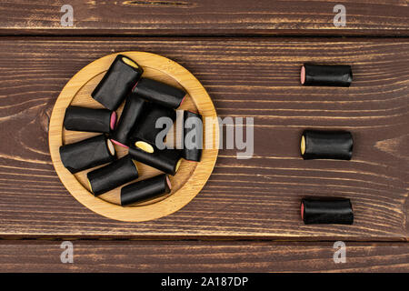 Menge ganz süßen schwarzen Lakritz Bonbons auf Bambus Untersetzer flatlay auf braunem Holz Stockfoto