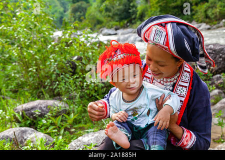 Red Dao ethnische Minderheit Frau und Baby (Dao), durch einen Fluss in Hoang Su Phi, Ha Giang Provinz, in der bergigen nordwestlichen Teil von Vietnam. Stockfoto