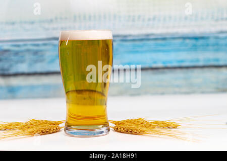 Pint Bier mit getrockneten Ohren Blumen von Weizen auf einem weißen Tisch mit einem bunten hölzernen Wand Textur Stockfoto