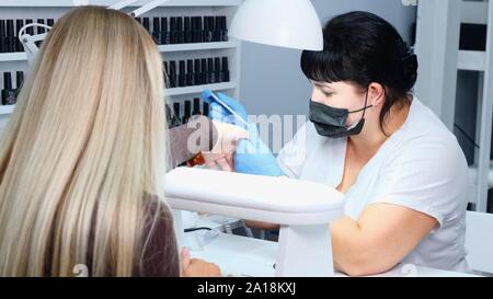 Closeup Schoß einer Frau in einem Nagelstudio, Maniküre, durch eine Kosmetikerin mit Nagelfeile. Frau erhalten Nagel Maniküre. Kosmetikerin Nägel in eine Datei Stockfoto