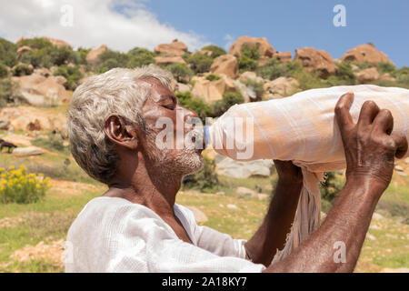 Maski, Indien, 21. September 2019: In der Nähe von durstig Landwirt mann Trinkwasser aus Kunststoff Flasche mit Tuch für die Kühlung während des heißen sonnigen abgedeckt Stockfoto