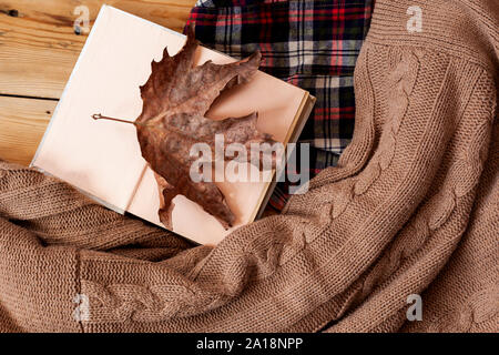 Herbst Hintergrund. Buch und einem großen trockenen Blatt geöffnet. Gestrickte Pullover auf Holz. Herbstliche Stimmung Stockfoto