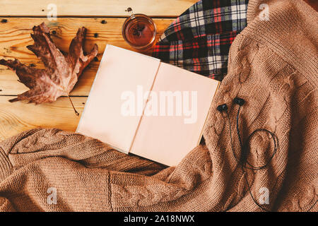 Herbst Hintergrund. Buch, Blatt und gestrickte Pullover geöffnet. Eine Tasse heißen Tee, strickschal auf hölzernen Tisch. Herbst wärmendes Getränk. Ansicht von oben. Kopieren spa Stockfoto