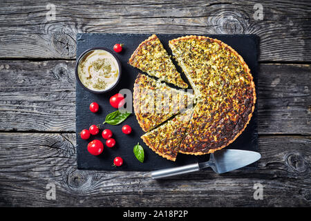 In Scheiben geschnitten Quiche mit grünen Zwiebeln und Spinat auf schwarzem Schiefer Fach mit herzhaften Dip und Tomaten, Ansicht von oben, flatlay Stockfoto