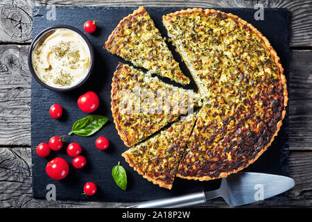 Close-up von geschnittenen Quiche mit grünen Zwiebeln und Spinat auf schwarzem Schiefer Fach mit herzhaften Dip und Tomaten, Ansicht von oben, flatlay Stockfoto