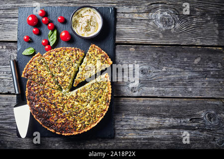 In Scheiben geschnitten Quiche mit grünen Zwiebeln und Spinat auf schwarzem Schiefer Fach mit herzhaften Dip und Tomaten, Ansicht von oben, flatlay, freier Speicherplatz Stockfoto