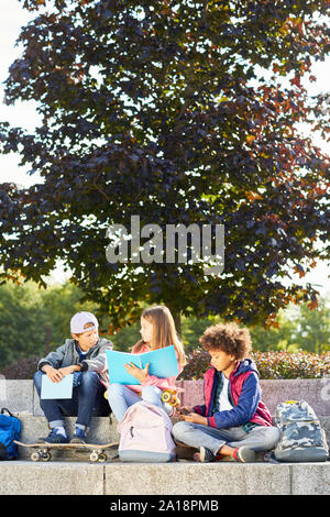 Gruppe von Freunden sitzen auf der Treppe mit Büchern und Skateboards und reden miteinander im Freien Stockfoto