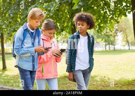 Gruppe von Schulkindern, die lässige Kleidung zusammen gehen in den Park und die Nutzung von Mobiltelefonen Stockfoto