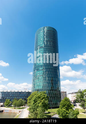 Der Westhafen Tower in Frankfurt am Main mit Bäumen in der Front an einem bewölkten Tag Stockfoto