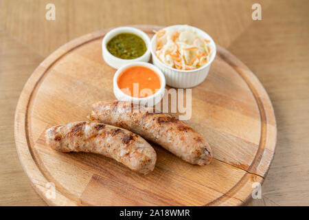 Gegrillte Würstchen. Serviert auf einem Holzbrett. Grill Restaurant Menü, eine Reihe von Fotos von verschiedenen Fleischsorten. Sauerkraut und zwei Saucen Stockfoto