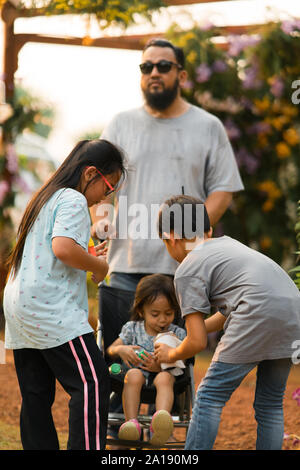 Asiatische Familie im Park. Kleinkinder trinken von Bruder. Stockfoto