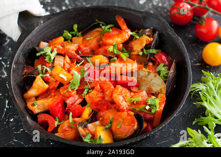 Meeresfrüchte cioppino Eintopf mit Garnelen, Jakobsmuscheln, Venusmuscheln, Muscheln und Fisch in der Pfanne auf Schwarzen Tisch, serviert mit Gemüse Stockfoto