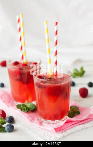 Frische rosa Limonade mit Himbeere, Preiselbeere, Erdbeere, Apfel, Limette mit Minze auf weißem rustikalen Tisch dekoriert Stockfoto